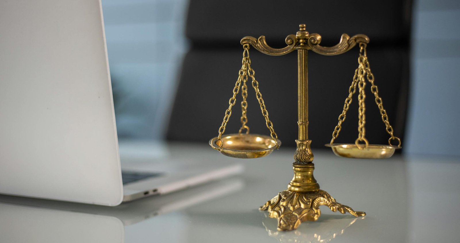 Golden justice scales on a desk beside a laptop, symbolizing law and balance.