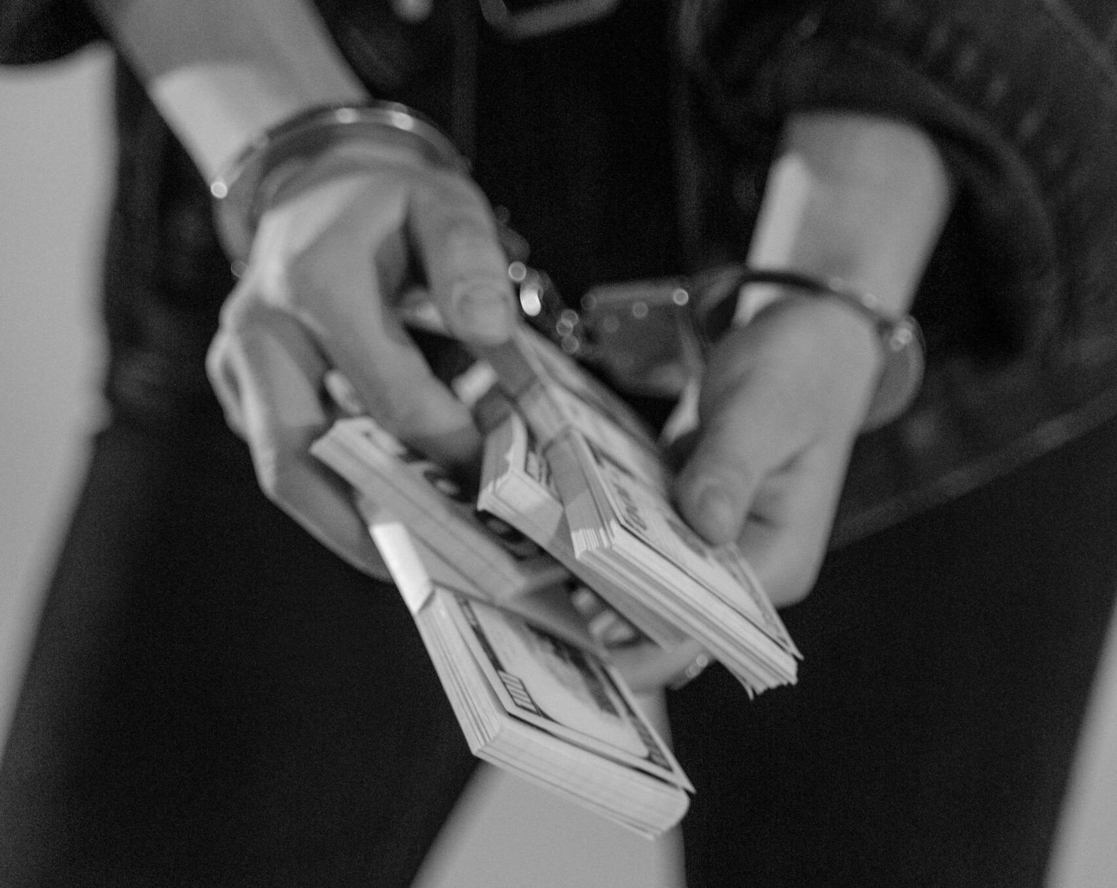 Grayscale image of handcuffed hands holding bundles of cash, emphasizing financial crime.